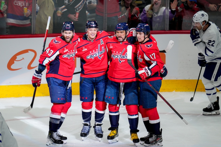 Four Washington Capitals players, including a team veteran, celebrate together on the ice after a successful play, showing camaraderie and excitement during the game.