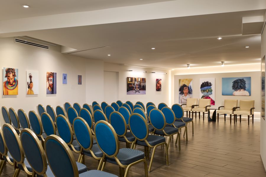  A contemporary meeting room at The Ven at Embassy Row, featuring rows of blue chairs, modern artwork on the walls, and a cozy setup for panel discussions or presentations.