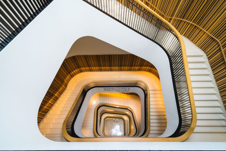 A top-down view of a modern spiral staircase with sleek, curved railings and warm lighting, creating a geometric, architectural pattern.