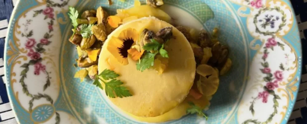 Close-up of a beautifully plated cheesecake with pistachios and edible flowers on an ornate blue and white dish